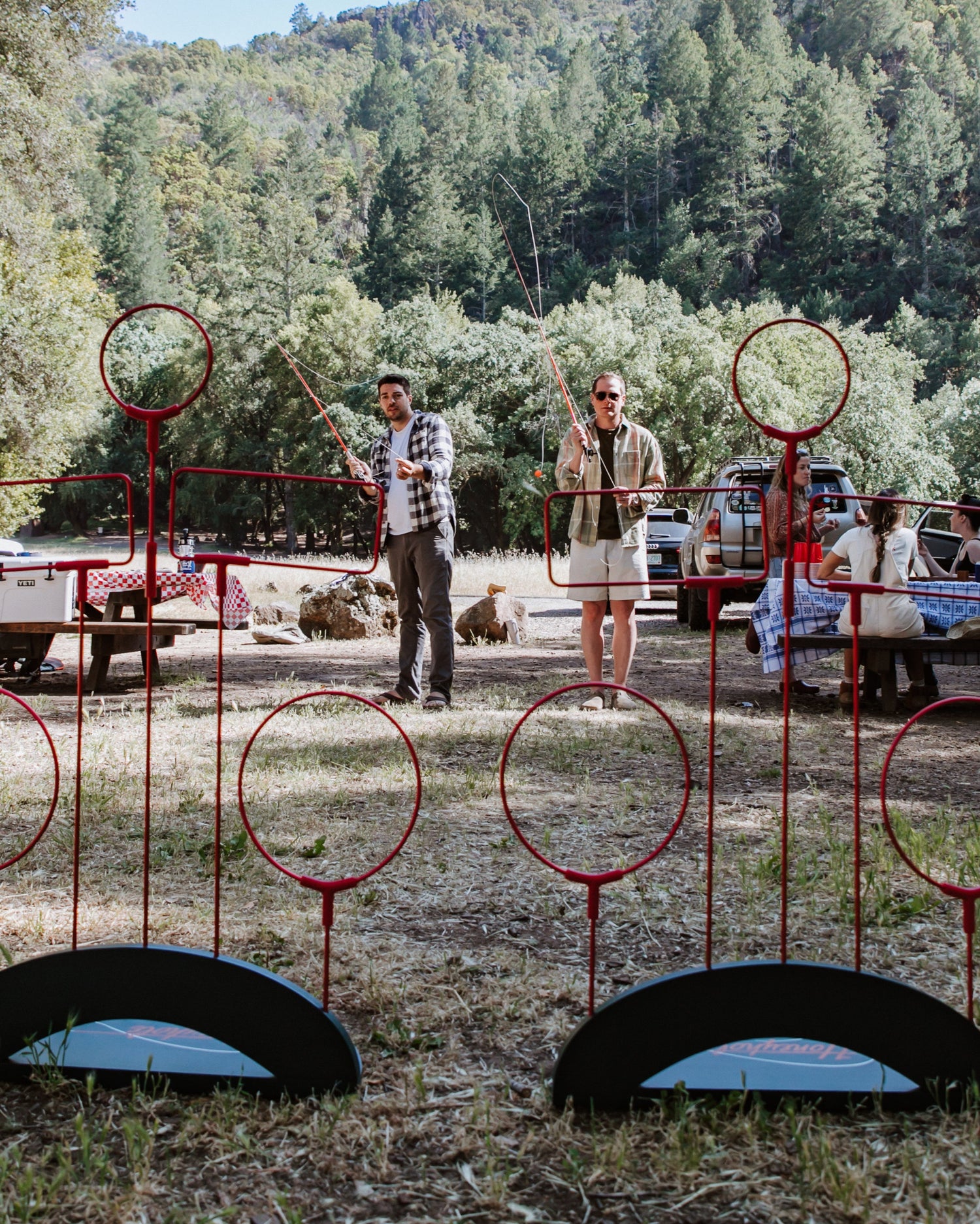 Outdoor scene with people and red metal game equipment in a forested area.